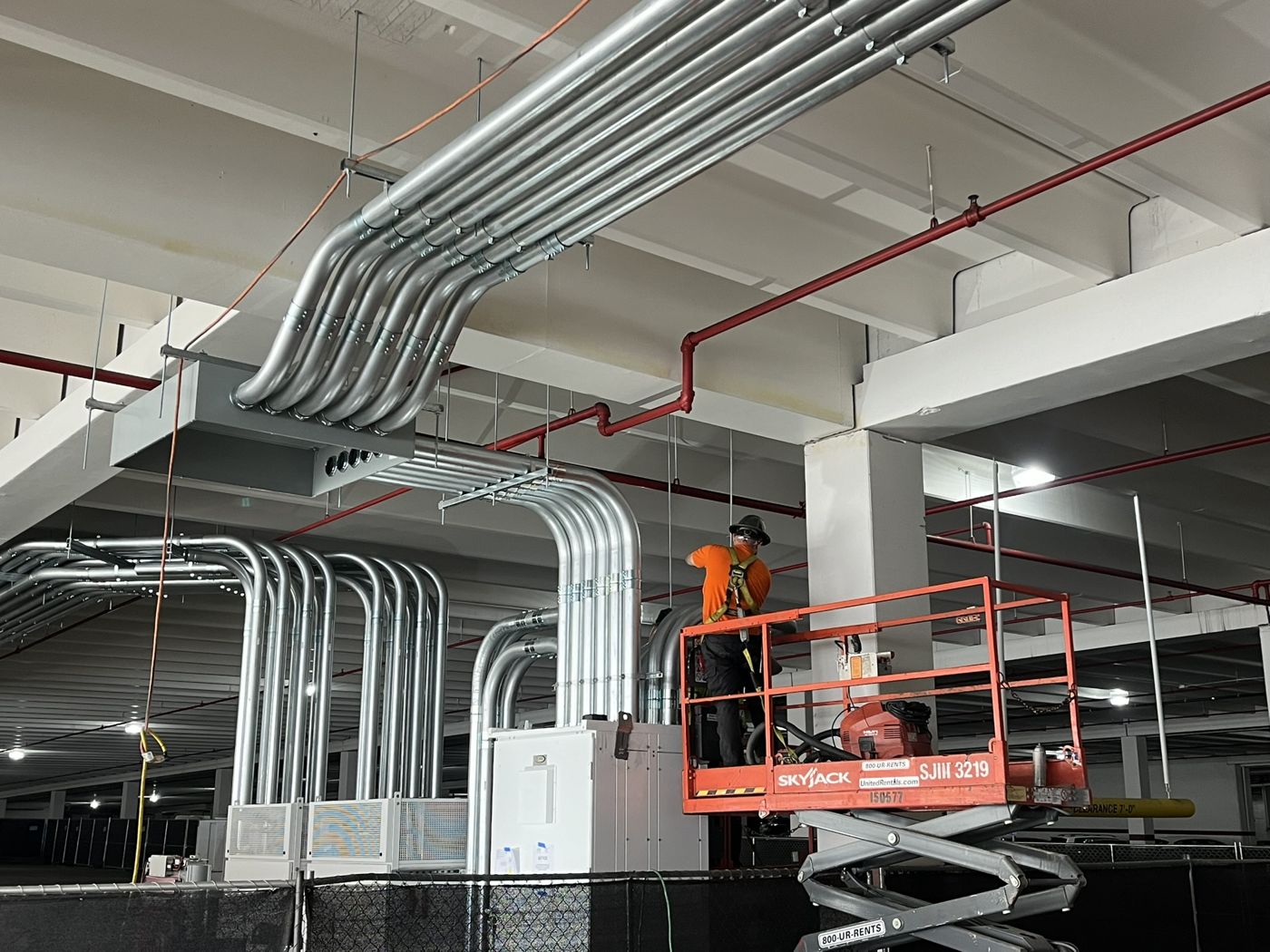 Electrician on a scissor lift installing an overhead conduit bank in a parking structure